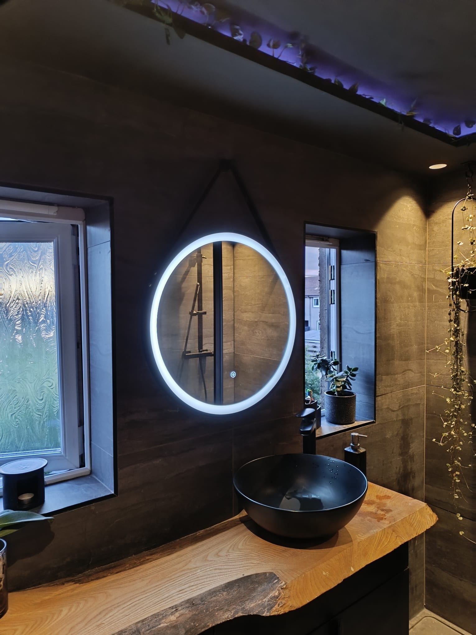 Bathroom with a round backlit LED mirror, a plant-lined LED cove and warm downlights