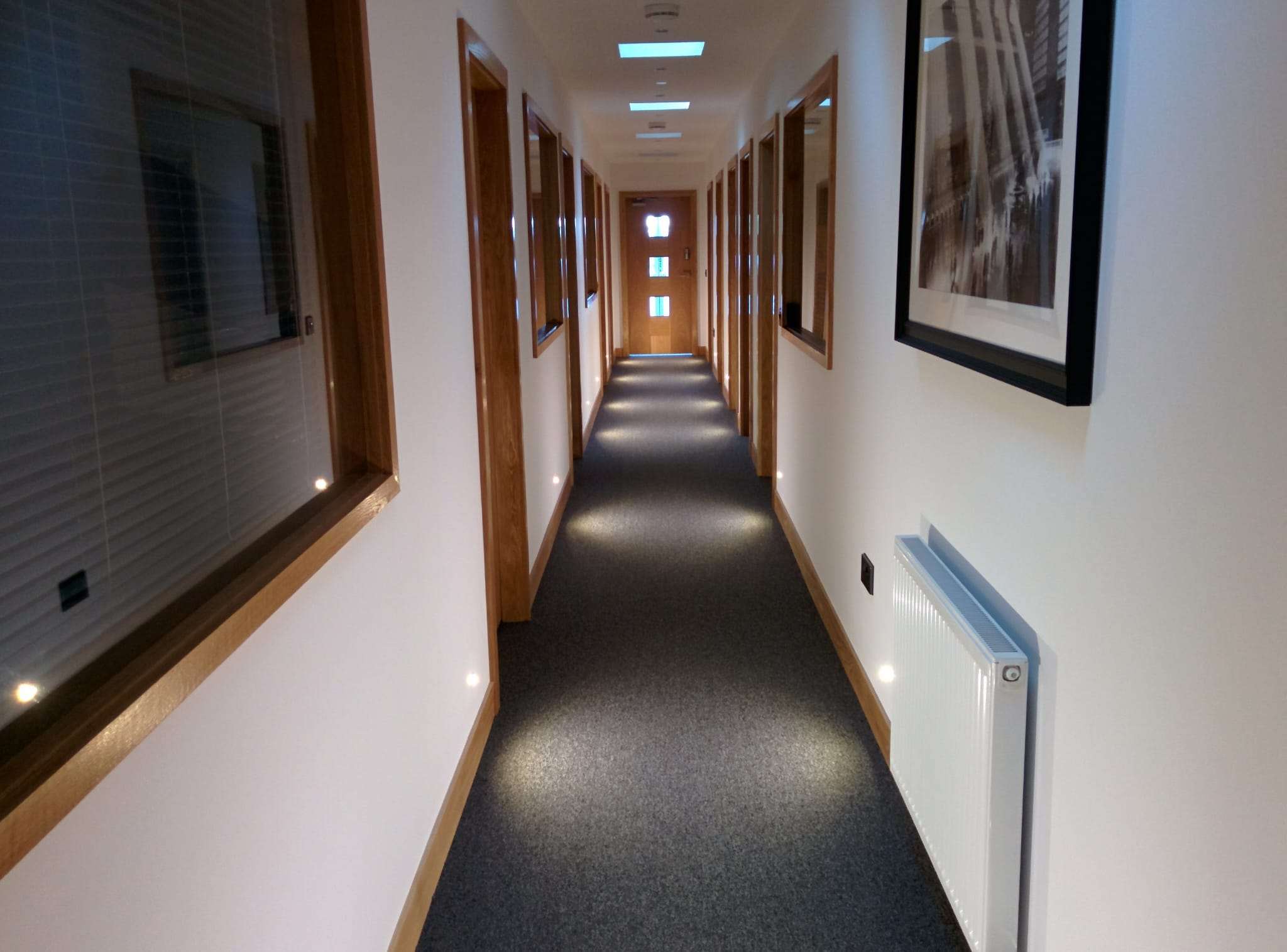 Office corridor with oak-framed glazing, recessed ceiling lights and LED floor washers along the skirting