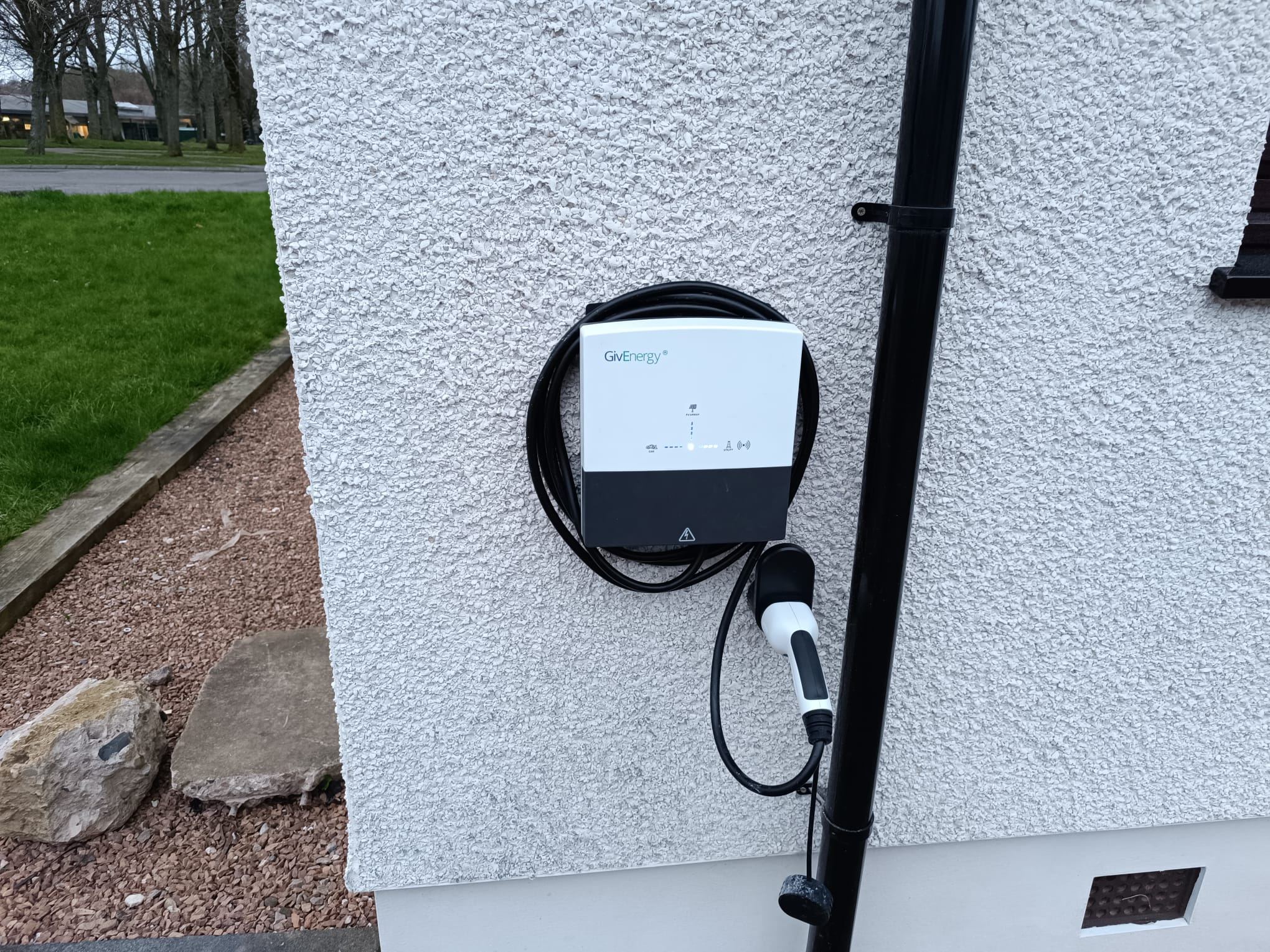 GivEnergy home EV charger with its tethered cable coiled, mounted on a white rendered wall