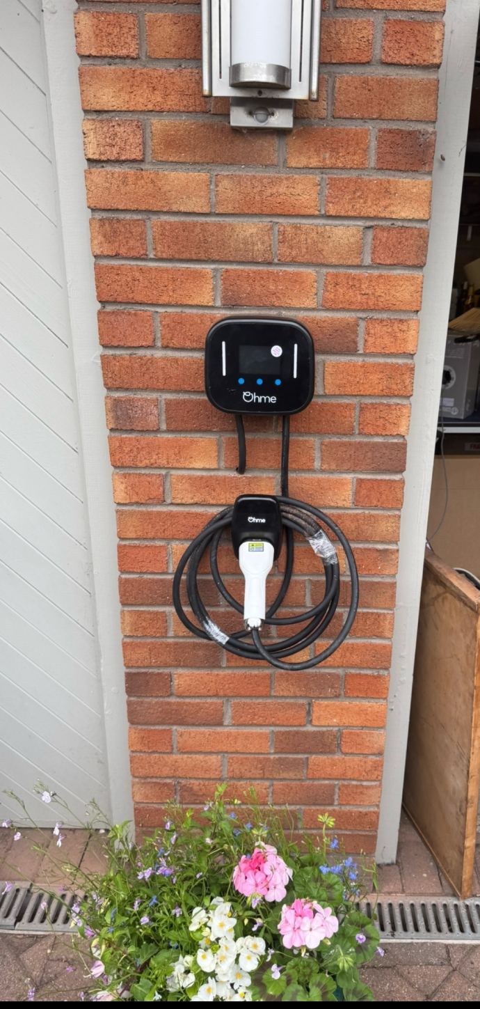 Ohme Home Pro EV charger with tethered cable hung on a brick pillar beside a garage door